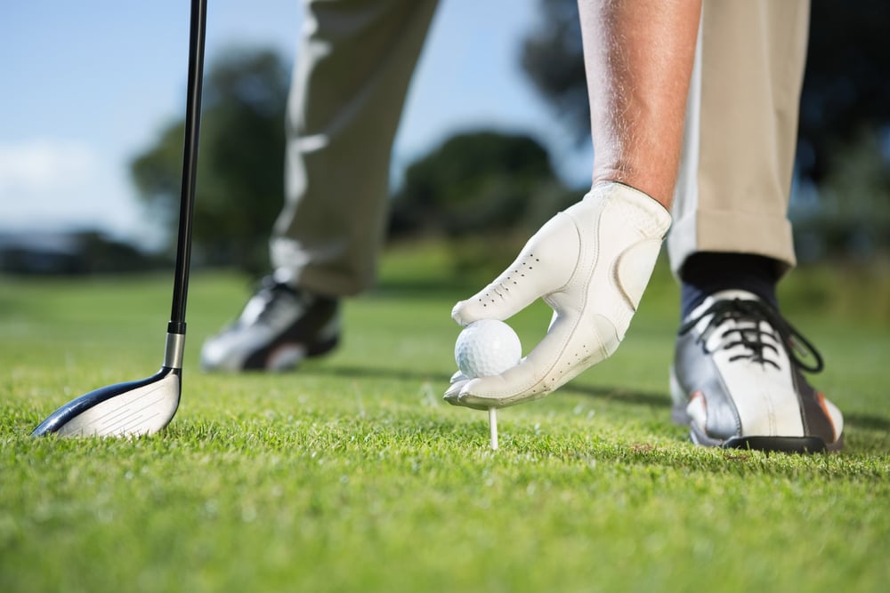 Golfer placing golf ball on tee on a sunny day at the golf course