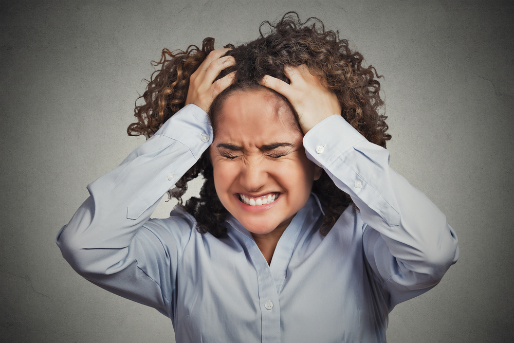 Frustrated stressed young woman. Headshot unhappy overwhelmed girl having headache bad day pulling her hair out isolated on grey wall background. Negative emotion face expression feelings perception