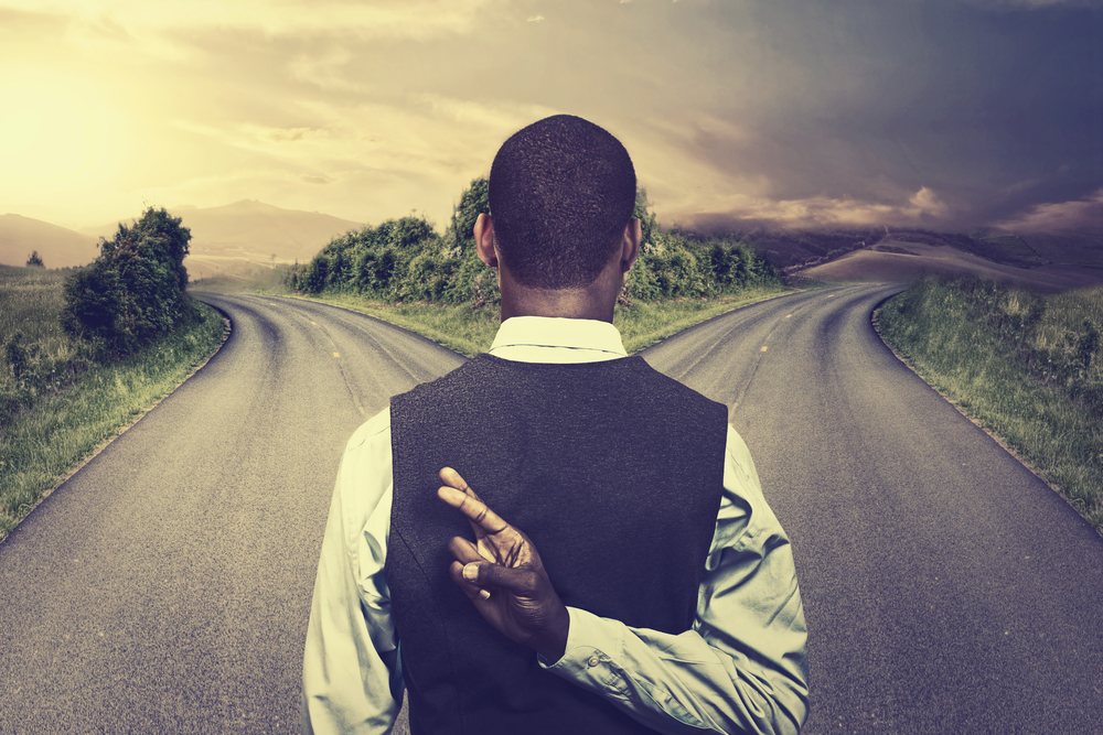 businessman in front of two roads crossing fingers hoping for best taking chance