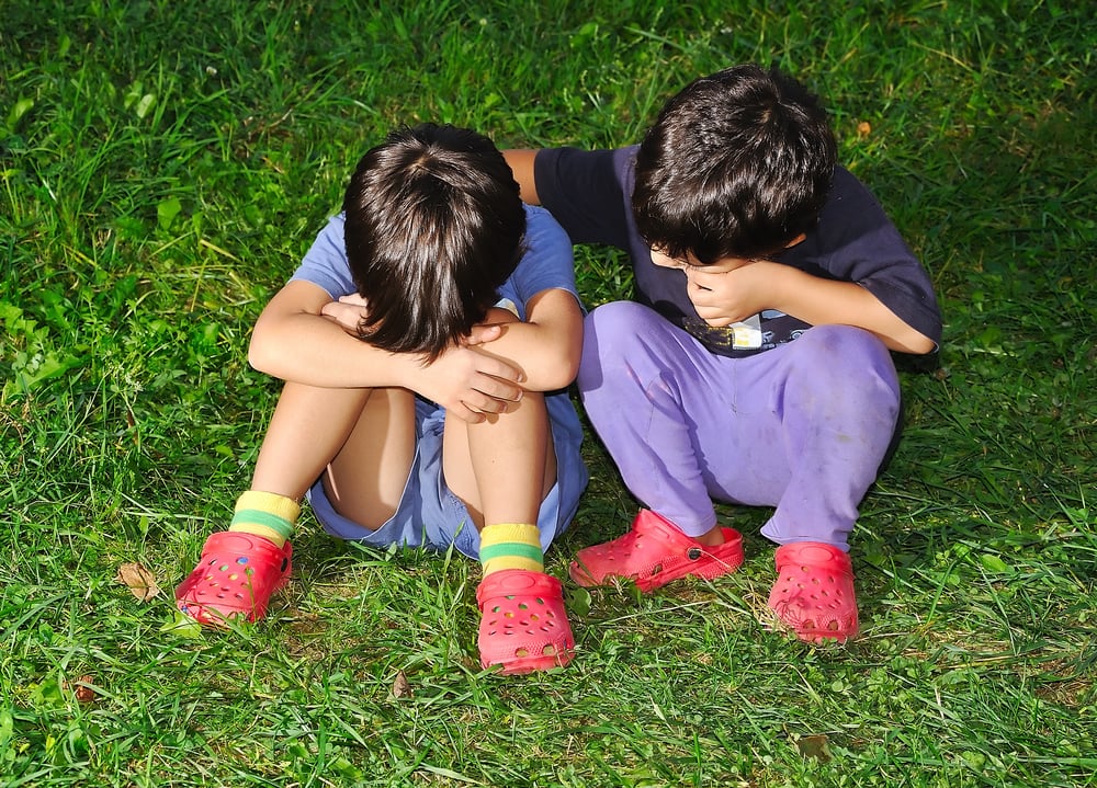 Two cute children sitting on ground, consoling each other